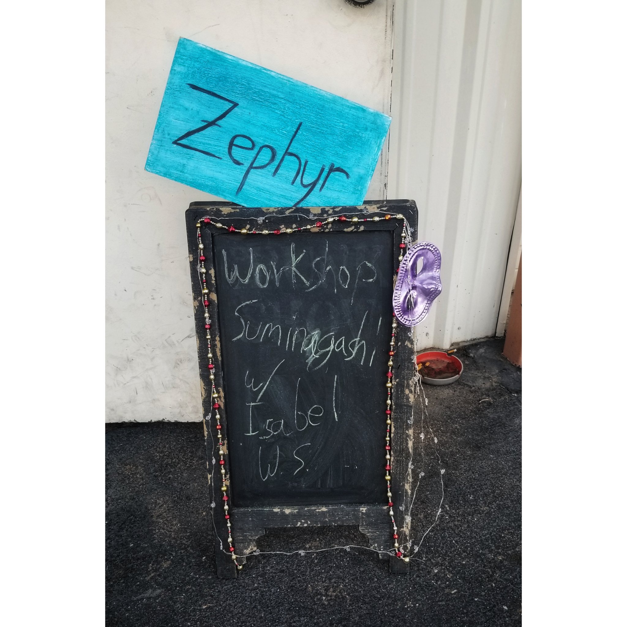 A sign with purple Mardi Gras mask, chalk writing, and Christmas lights. The sign says 