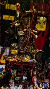Altar at the Vodoo Musuem in New Orleans, lots of mardi gras beads, photographs, and money. Text cards explain the different Orisha.
