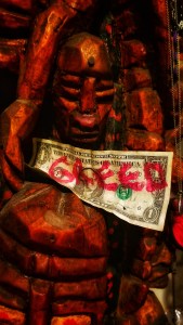 A red, carved face, and a dollar bill that says GREED in red