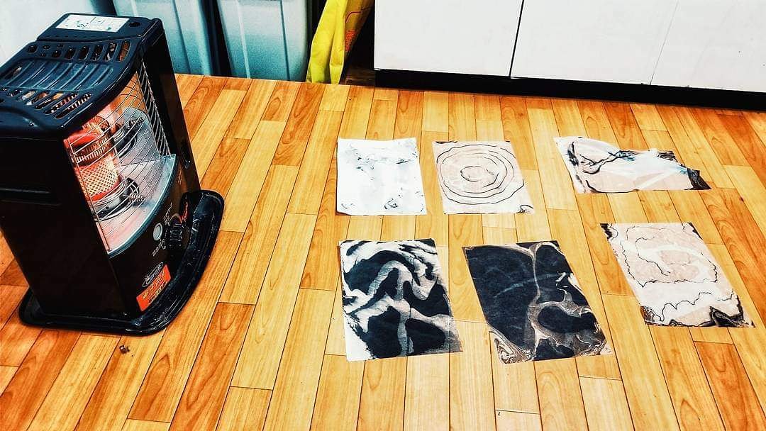 Suminagashi spread out on a wooden floor in front of a kerosene heater